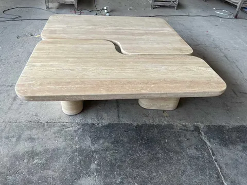 cream-beige stone coffee table, with twin supporting bases and linear travertine grain, in a workshop