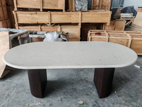 cream-beige stone dining table, with twin supporting bases and a speckled texture, in a workshop