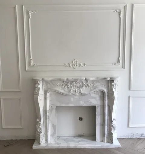 White Volakas marble fireplace surround, with carved scrollwork and fine veining, in a furnished room