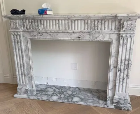Arabescato Corchia marble fireplace surround, with a straight recessed opening and fine veining, in a furnished room