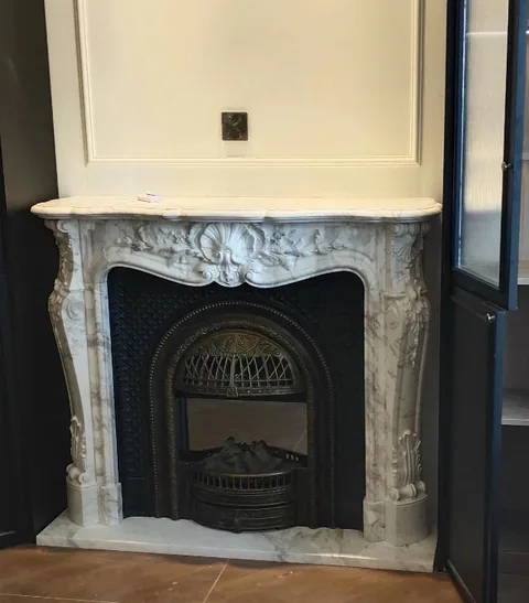 White Volakas marble fireplace surround, with carved scrollwork and fine veining, in a furnished room