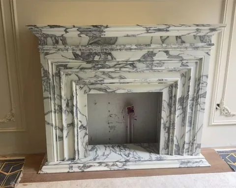 Arabescato Corchia marble fireplace surround, with stepped tiers and bold veining, in a furnished room