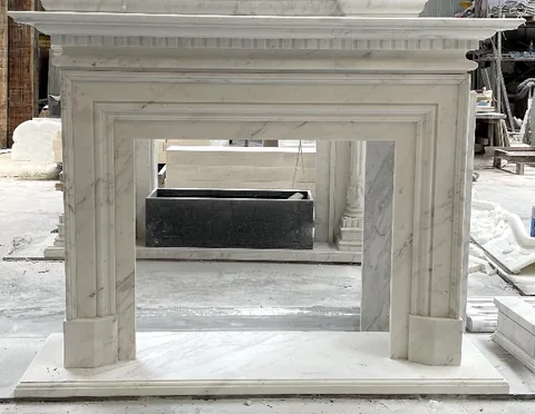 White Volakas marble fireplace surround, with stepped tiers and fine veining, in a workshop