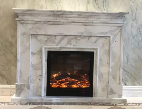 White Volakas marble fireplace surround, with stepped tiers and fine veining, in a furnished room