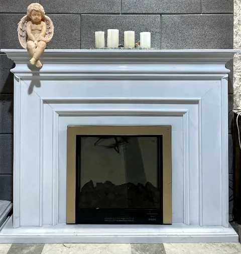 White Volakas marble fireplace surround, with stepped tiers and a plain surface, in a furnished room
