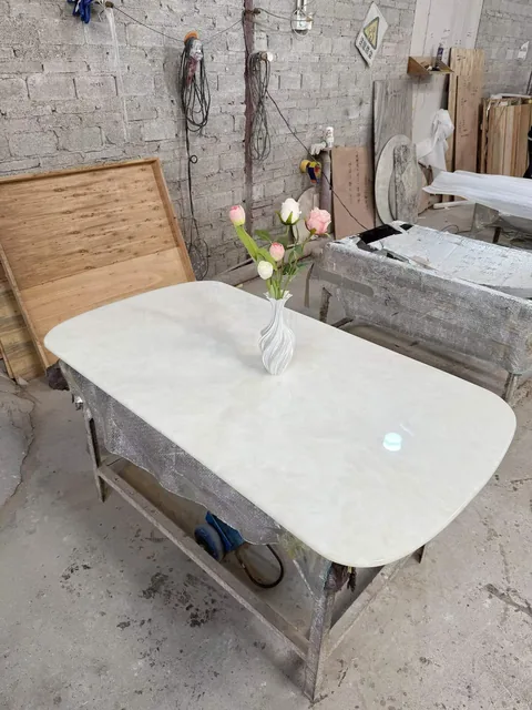 white stone dining table, with cloudy mottling and a reflective finish, in a workshop