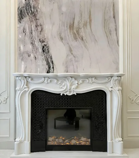 White Volakas marble fireplace surround, with carved scrollwork and bold veining, in a furnished room