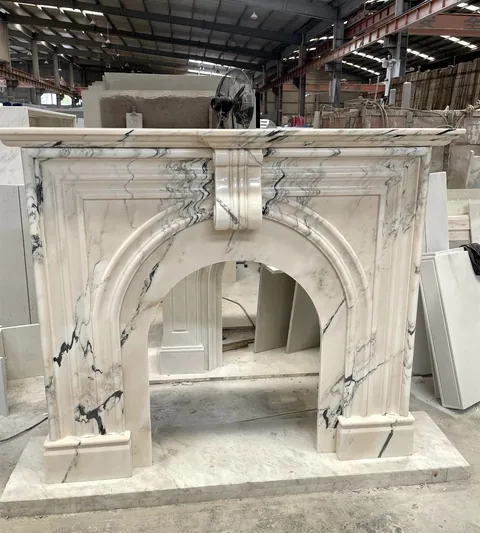 White Volakas marble fireplace surround, with an arched opening and bold veining, in a workshop