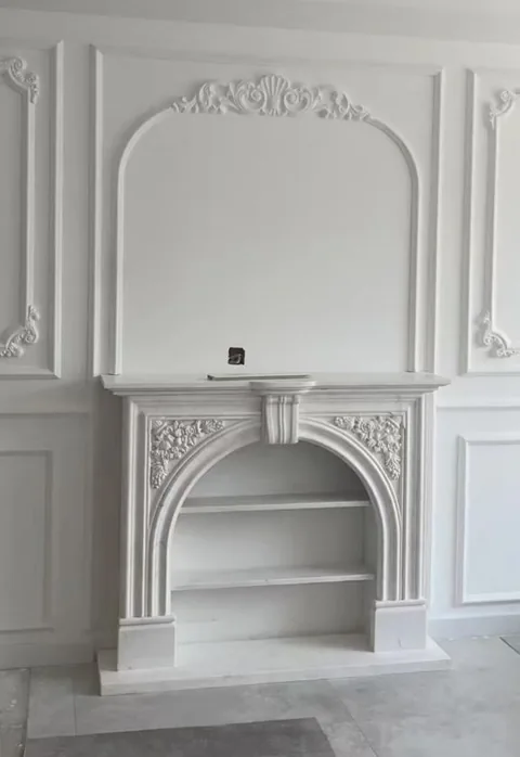 White Volakas marble fireplace surround, with an arched opening and a plain surface, against a pale background