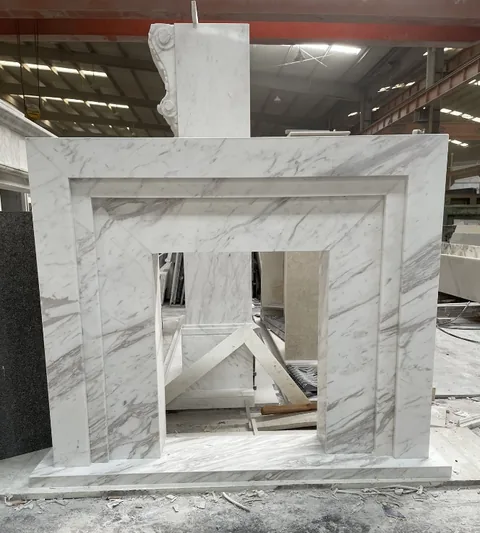 White Volakas marble fireplace surround, with stepped tiers and fine veining, in a workshop