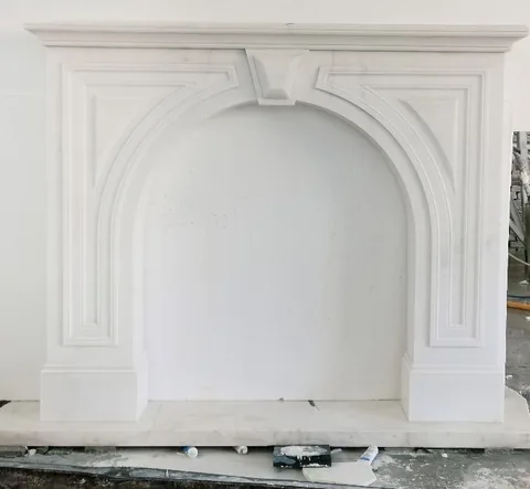 White Volakas marble fireplace surround, with an arched opening and fine veining, in a workshop