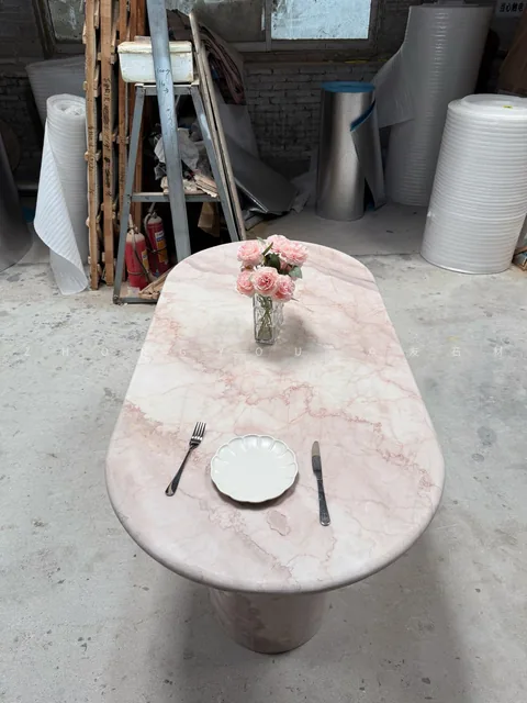 rose-red stone dining table, with a central pedestal base and fine veining, in a workshop