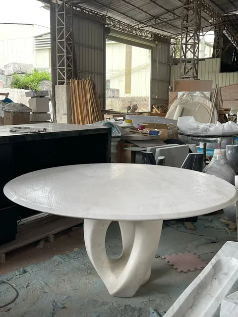 white stone dining table, with a round top and fine veining, in a workshop