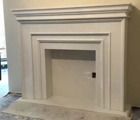 White Volakas marble fireplace surround, with stepped tiers and a plain surface, in a workshop
