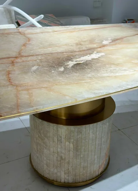 cream-beige stone dining table, with a central pedestal base and bold veining, in a furnished room
