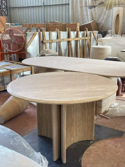cream-beige stone dining table, with a round top and cloudy mottling, in a workshop