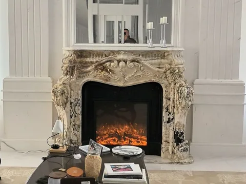 White Volakas marble fireplace surround, with carved scrollwork and bold veining, in a furnished room