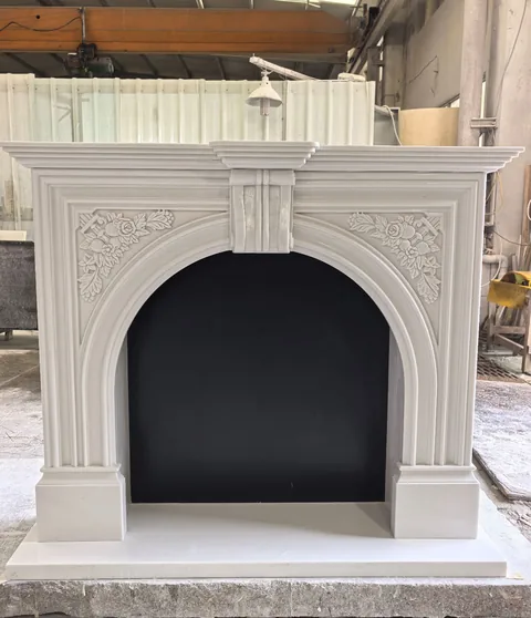 White Volakas marble fireplace surround, with an arched opening and a plain surface, in a workshop