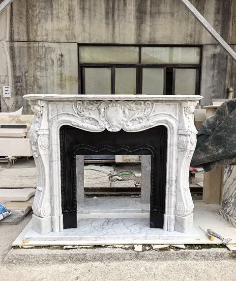 White Volakas marble fireplace surround, with carved scrollwork and fine veining, in a workshop