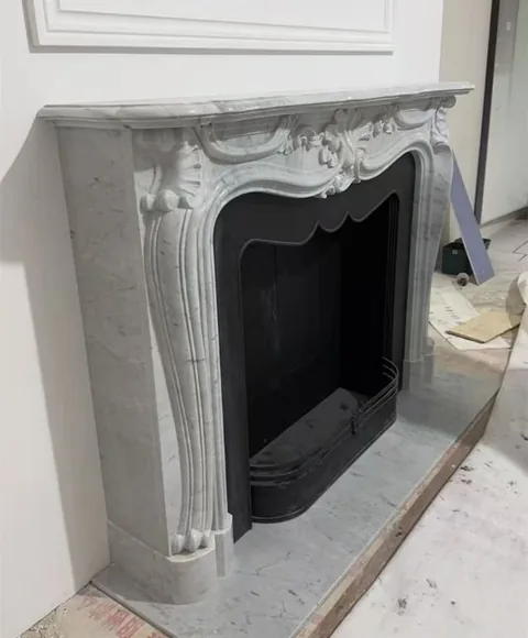 White Volakas marble fireplace surround, with carved scrollwork and fine veining, in a workshop