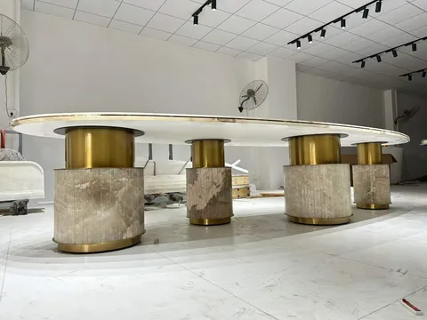 cream-beige stone dining table, with an oval top and linear travertine grain, in a workshop