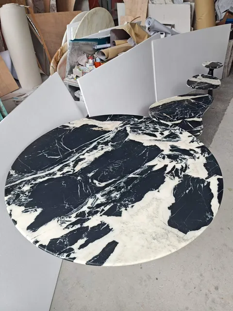 black stone dining table, with a round top and bold veining, in a workshop