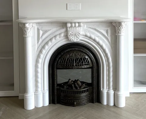 White Volakas marble fireplace surround, with an arched opening and fine veining, in a furnished room