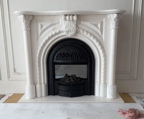 White Volakas marble fireplace surround, shown from a frontal view with workshop equipment nearby