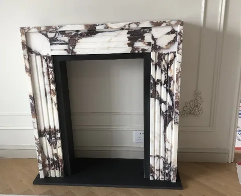 White Volakas marble fireplace surround, with a straight recessed opening and bold veining, in a furnished room