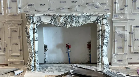 White Volakas marble fireplace surround, with carved scrollwork and bold veining, in a workshop