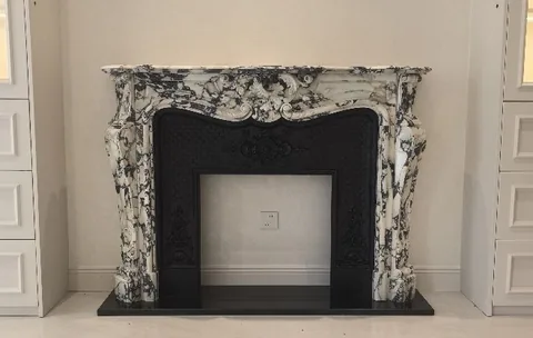 White Volakas marble fireplace surround, with carved scrollwork and bold veining, against a pale background