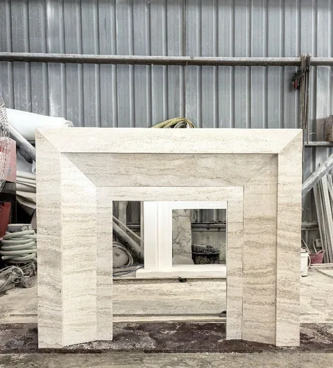 White Volakas marble fireplace surround, with stepped tiers and linear travertine grain, in a workshop