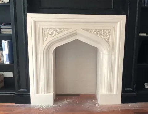 White Volakas marble fireplace surround, with an arched opening and a plain surface, in a furnished room