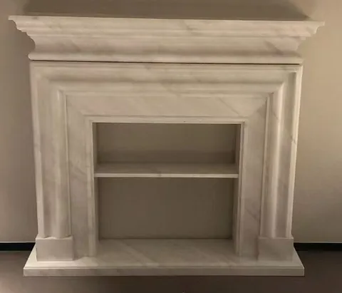 White Volakas marble fireplace surround, with stepped tiers and fine veining, on a plain backdrop