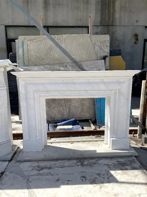White Volakas marble fireplace surround, shown from a frontal view with workshop equipment nearby