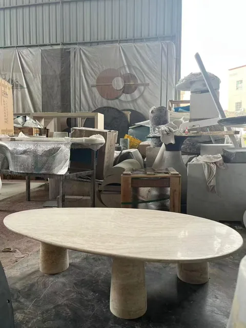 cream-beige stone coffee table, with an oval top and fine veining, in a workshop