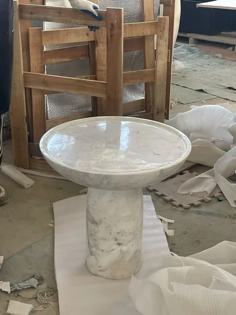 white stone coffee table, with a central pedestal base and fine veining, in a workshop