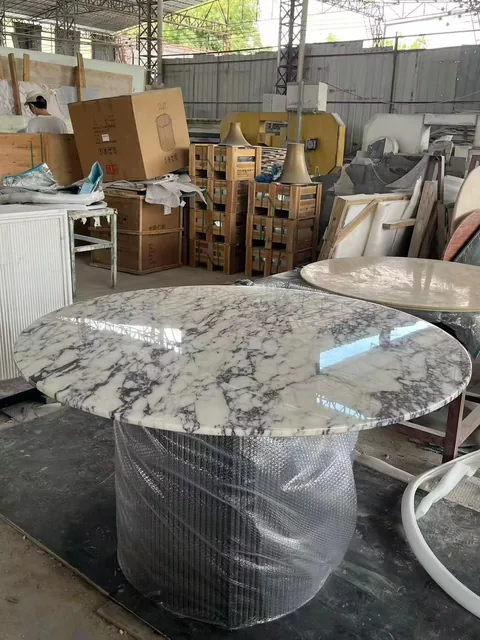 white stone dining table, with a round top and bold veining, in a workshop