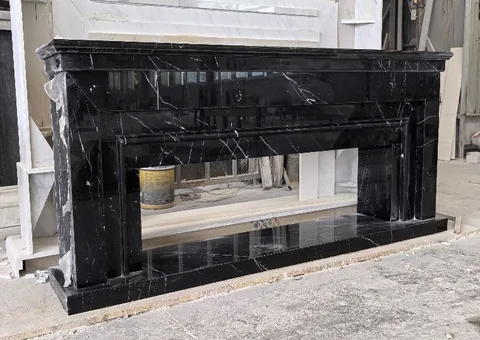White Volakas marble fireplace surround, with fine veining, shown from an angled view with workshop equipment nearby