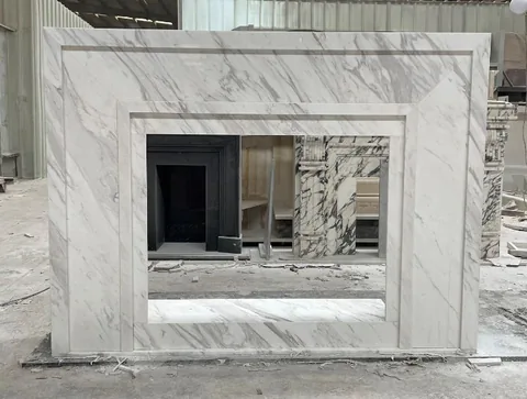 White Volakas marble fireplace surround, with fine veining, showing a single main form with workshop equipment nearby
