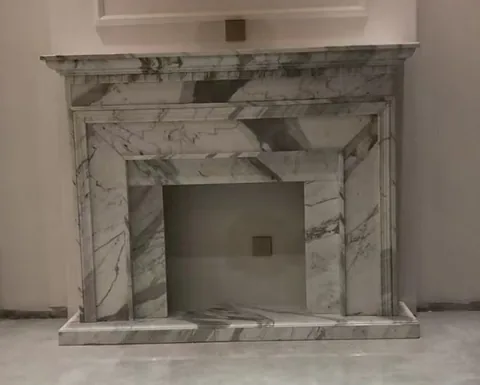White Volakas marble fireplace surround, with stepped tiers and bold veining, against a pale background
