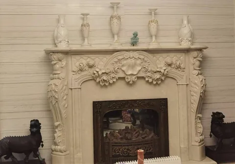 White Volakas marble fireplace surround, with carved scrollwork and linear travertine grain, in a furnished room
