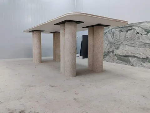 cream-beige stone dining table, with twin supporting bases and linear travertine grain, in a workshop