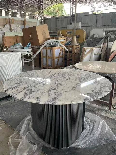 white stone dining table, with a round top and fine veining, in a workshop