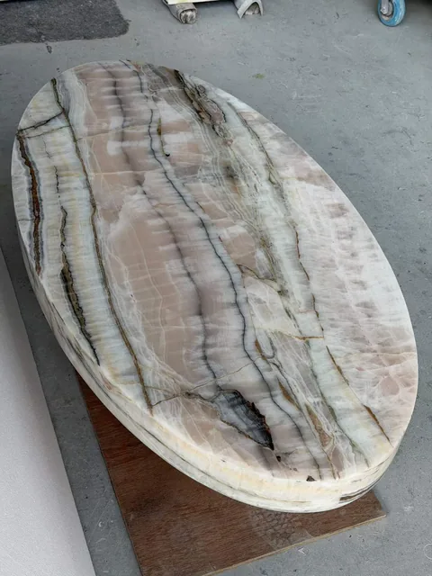 cream-beige stone coffee table, with an oval top and banded onyx-like striping, in a workshop