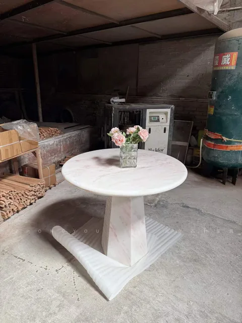 white stone dining table, with a round top and fine veining, in a workshop