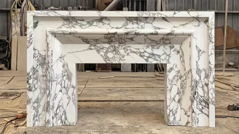 White Volakas marble fireplace surround, with stepped tiers and bold veining, in a workshop