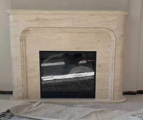 travertine fireplace surround, with an arched opening and linear travertine grain, against a pale background