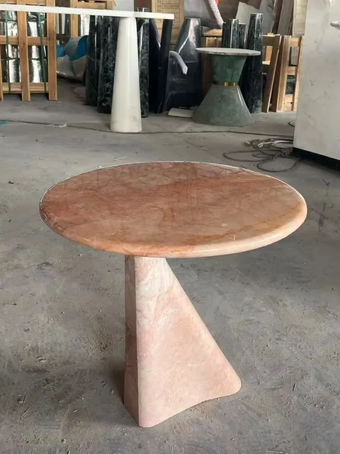 rose-red stone side table, with a round top and cloudy mottling, in a workshop