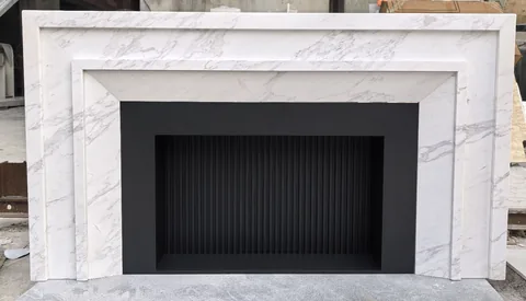 White Volakas marble fireplace surround, with fine veining and workshop equipment nearby